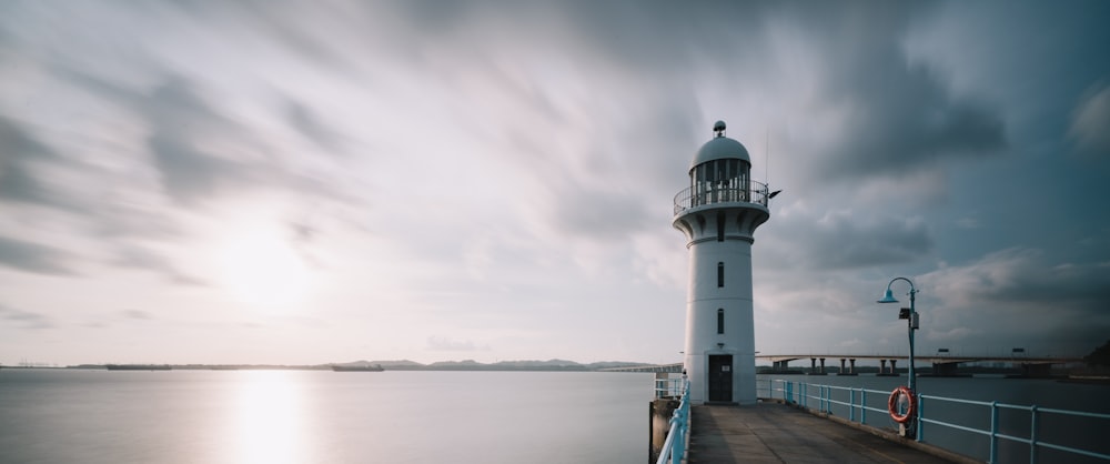 white and black lighthouse near body of water under cloudy sky during daytime