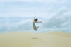 woman in white dress jumping on brown sand during daytime