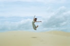 woman in white dress jumping on brown sand during daytime