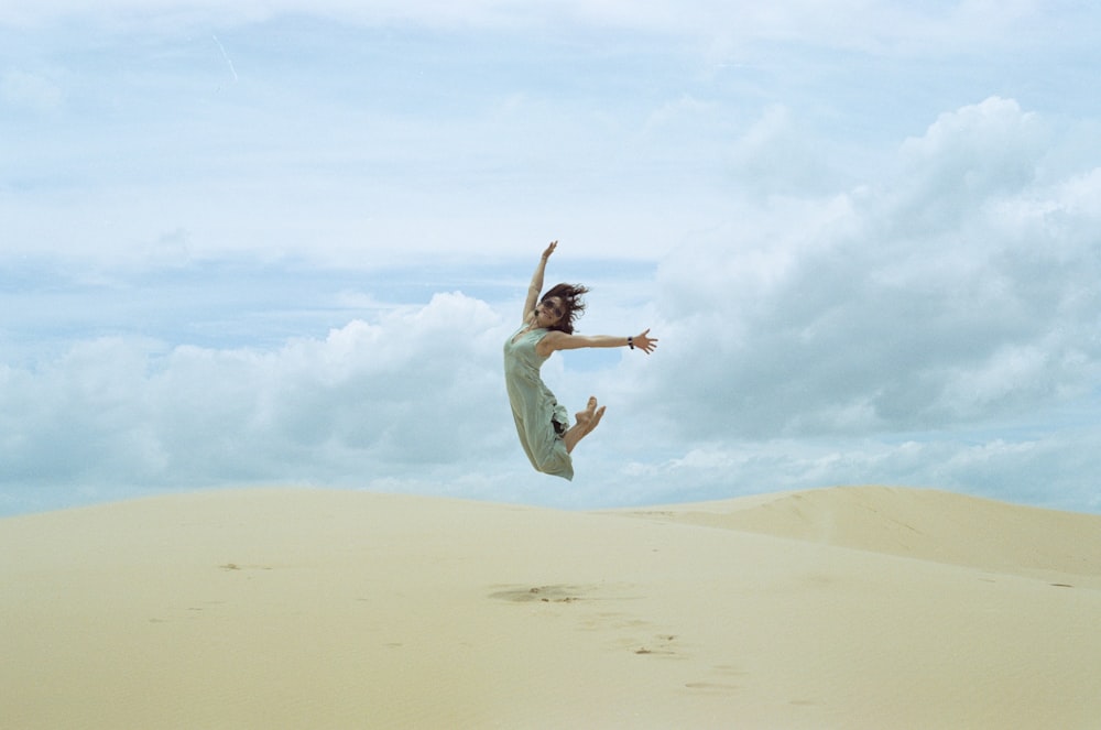 femme en robe blanche sautant sur le sable brun pendant la journée