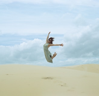 woman in white dress jumping on brown sand during daytime