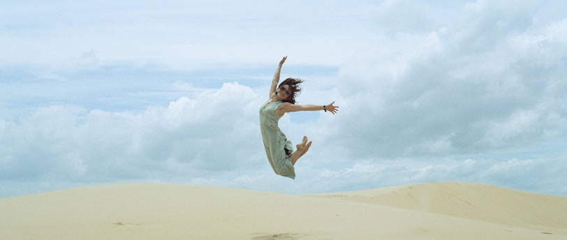 woman in white dress jumping on brown sand during daytime