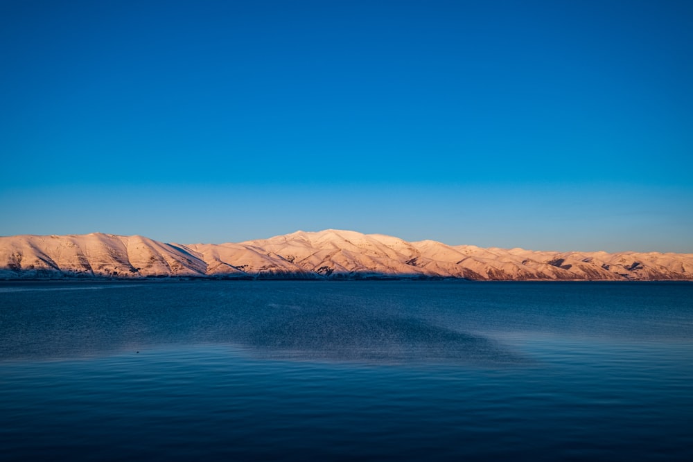 Mar azul cerca de la montaña marrón bajo el cielo azul durante el día