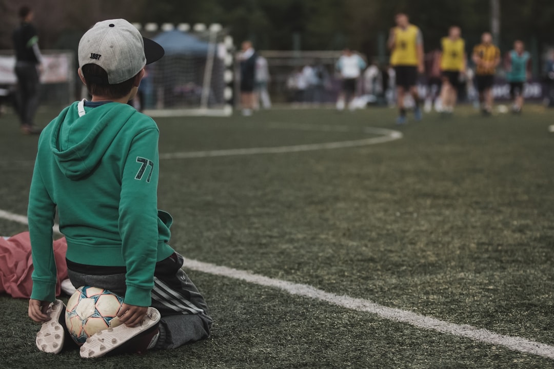 man in green and white long sleeve shirt and black pants sitting on green grass field