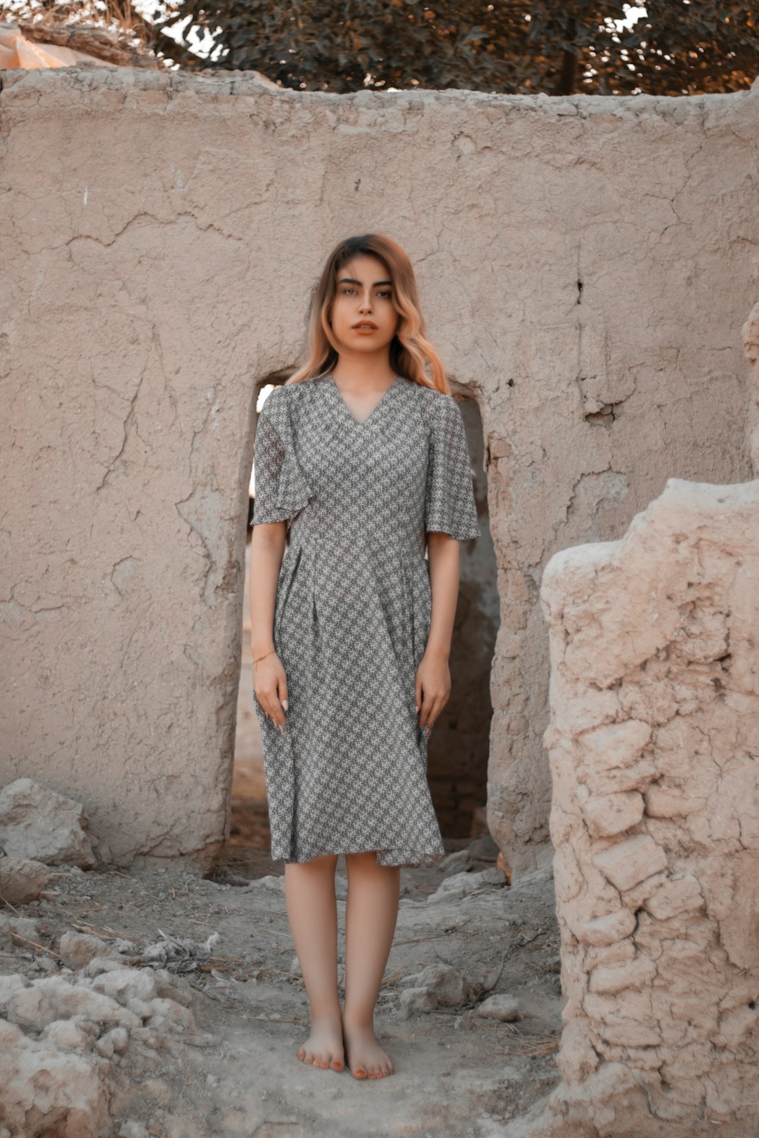 woman in gray and white dress standing beside brown wall