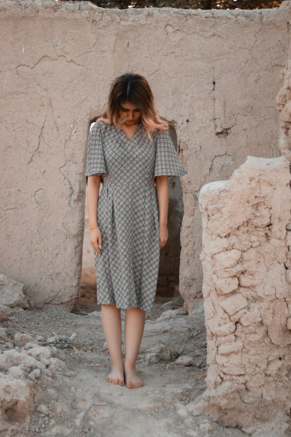 woman in black and white checkered dress standing beside brown concrete wall during daytime