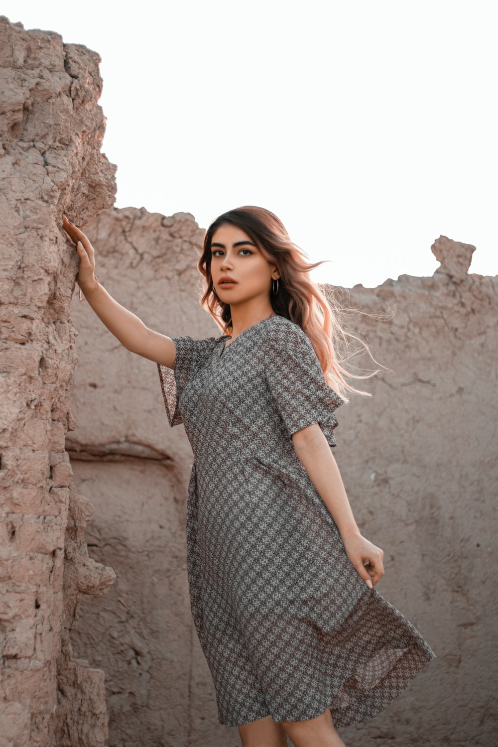 woman in black and white polka dot dress leaning on brown rock