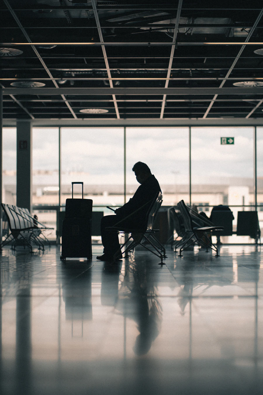 Lone traveler silhouetted beside a rolling suitcase, waiting in a near-empty terminal