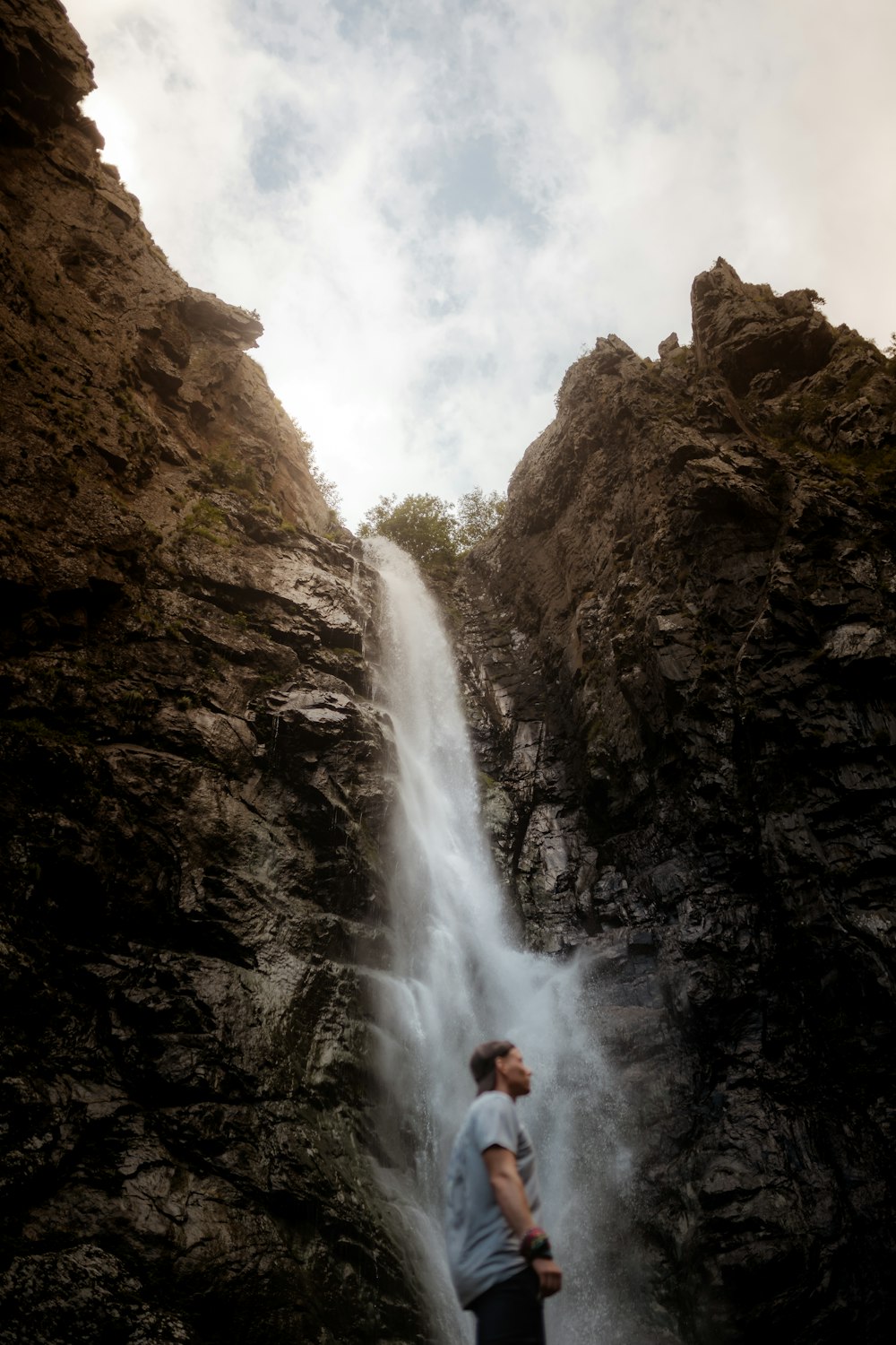 person in white shirt standing on rock near waterfalls during daytime