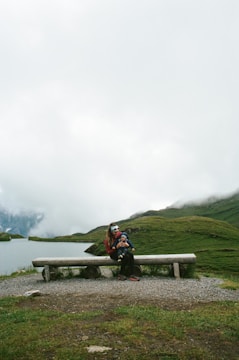 person in black jacket sitting on brown wooden bench on green grass field during daytime