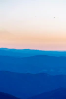 A serene watercolor landscape featuring soft blue mountains fading into a bright sky.