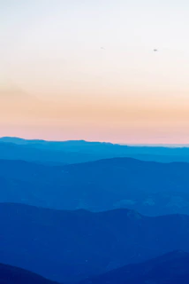 A serene watercolor landscape featuring soft blue mountains fading into a bright sky.