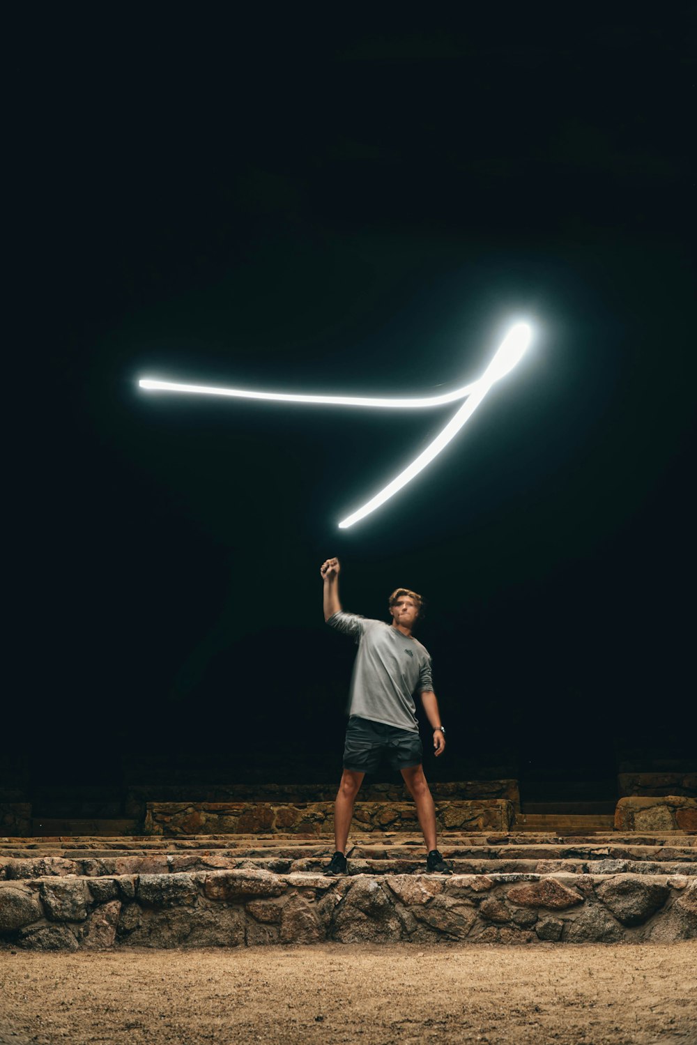 man in white t-shirt and black shorts standing on brown concrete bricks during nighttime