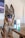A German Shepherd dog sits in a room, its tongue out and expression relaxed. In the foreground, there is a bottle and a box of CBD oil for pets labeled 'Resilience' on a wooden table. The background includes a blurry portion of a TV screen and indoor furniture.