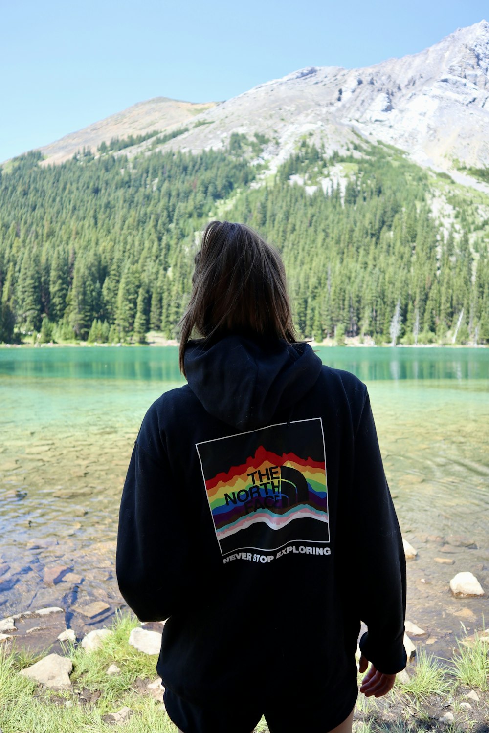 woman in black hoodie standing on gray sand near lake during daytime