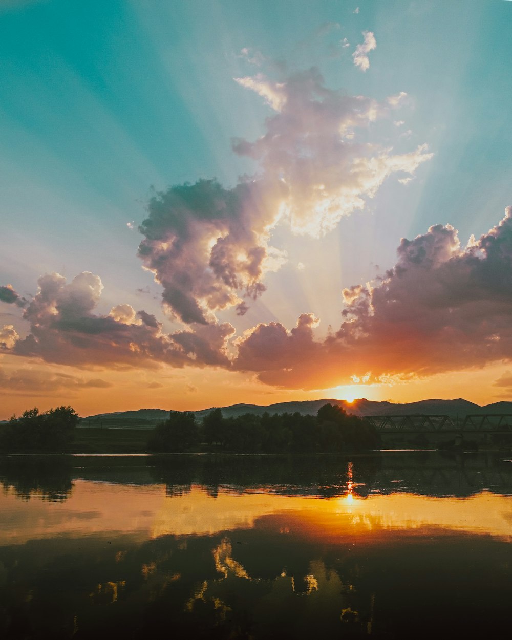 body of water near trees during sunset