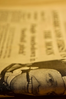 A close-up of a newspaper page with printed text and a low-resolution image of a man's face. The image is in a sepia tone, giving it a vintage look.