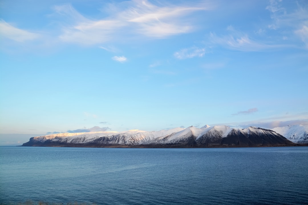 blue sea near snow covered mountain under blue sky during daytime