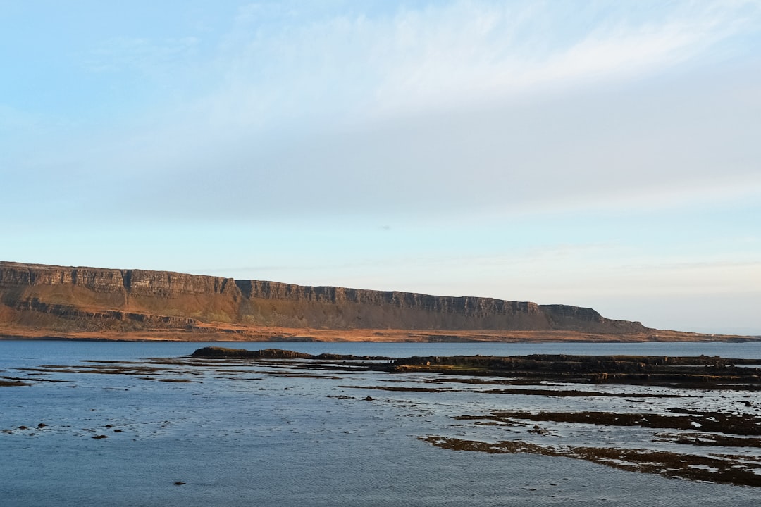 brown and green mountain beside body of water under white clouds during daytime