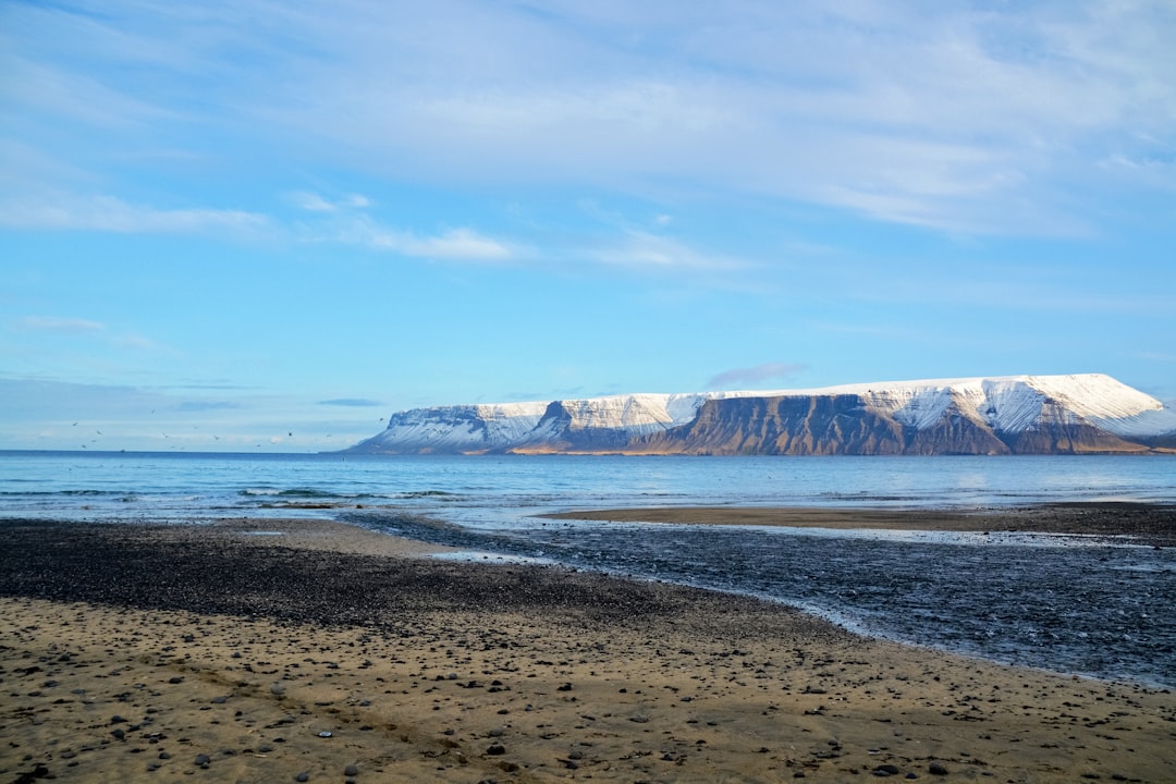 brown and white mountains beside body of water under blue sky during daytime