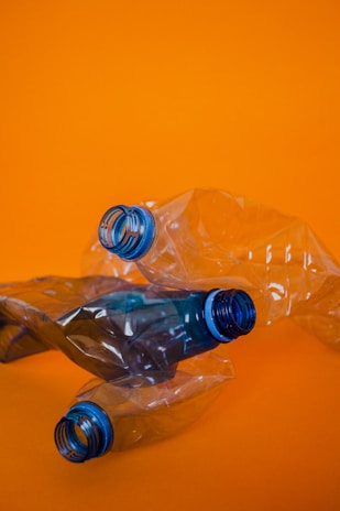 Three crumpled plastic bottles with blue caps are positioned against a bright orange background, creating a vivid contrast.