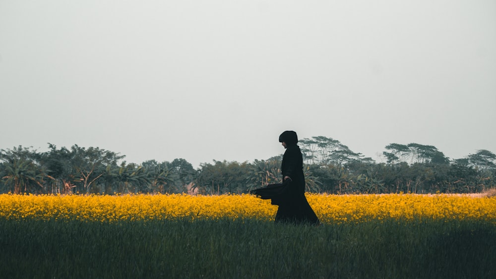 person in black coat standing on yellow flower field during daytime