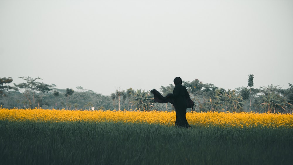 man in black jacket standing on yellow flower field during daytime