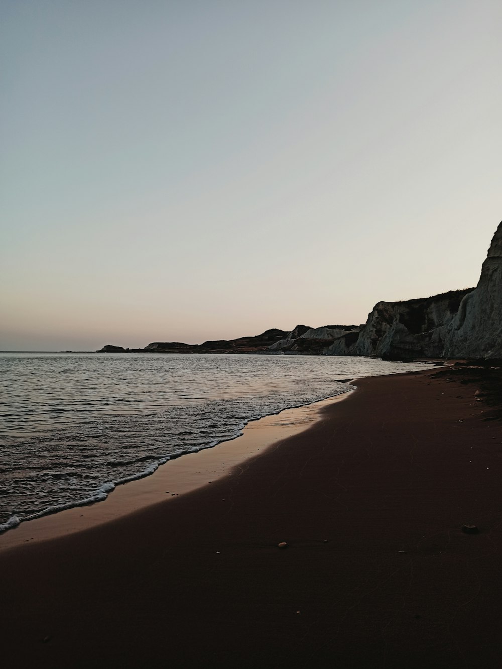 praia de areia marrom perto da montanha rochosa cinza durante o dia
