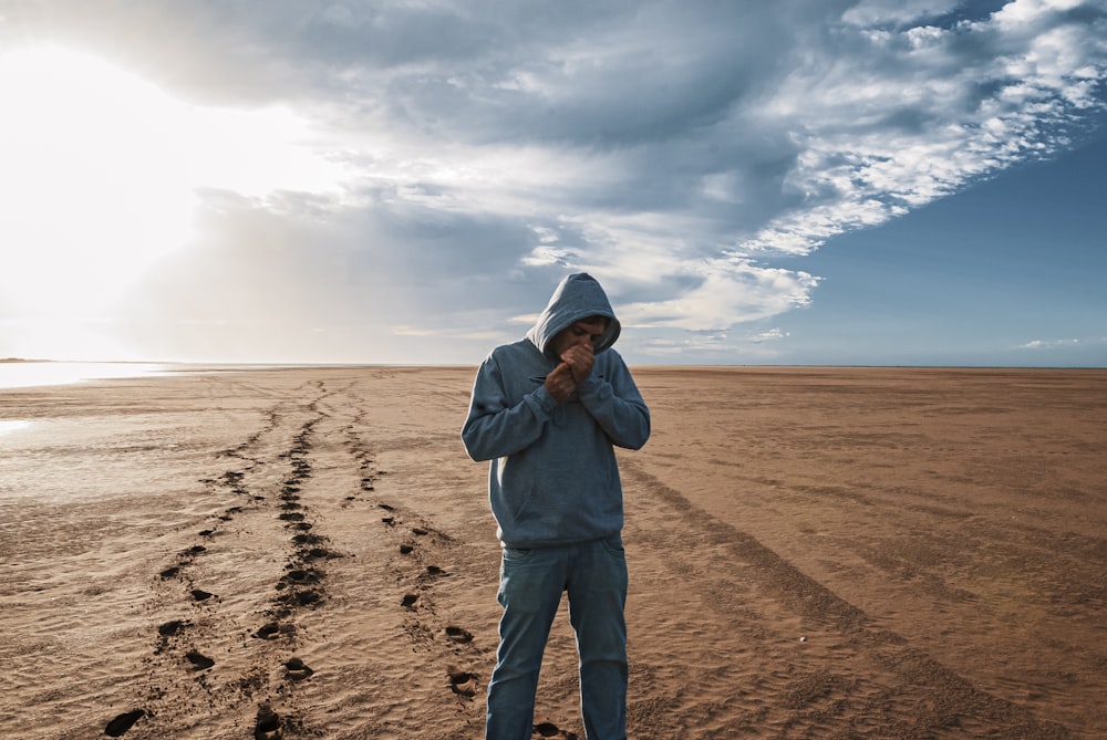 man in gray hoodie standing on brown sand under white clouds during daytime