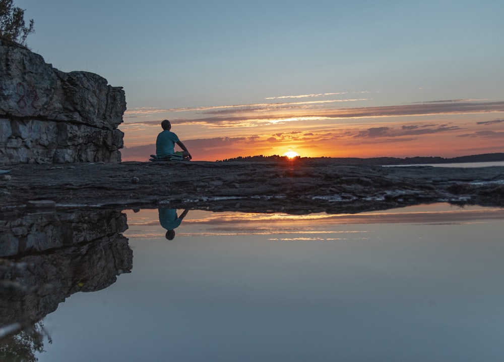 man in green shirt sitting on rock formation during sunset