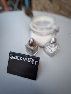 A small blackboard sign with white chalk that reads 'RESERVIERT' is placed on a light-colored table. Next to the sign, there are a few small glass containers, possibly for condiments.