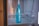 A blue bottle with the brand name Samsung written on it is placed inside a refrigerator. The interior of the fridge is mostly empty, with metal shelves visible in the background.
