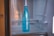 A blue bottle with the brand name Samsung written on it is placed inside a refrigerator. The interior of the fridge is mostly empty, with metal shelves visible in the background.