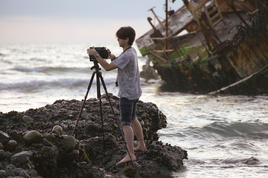 man in white shirt and blue and white plaid shorts holding camera