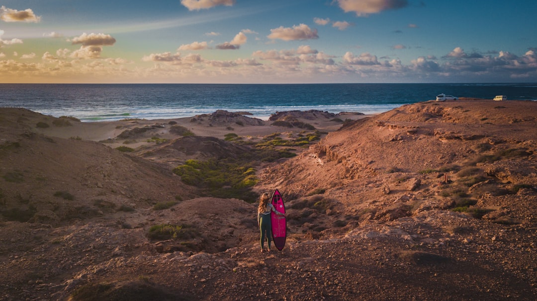 woman in blue and red backpack standing on brown rock formation near body of water during