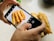 A person's hands holding a smartphone capturing a photo of a plate with several long, golden-brown fried dough sticks on a speckled countertop.