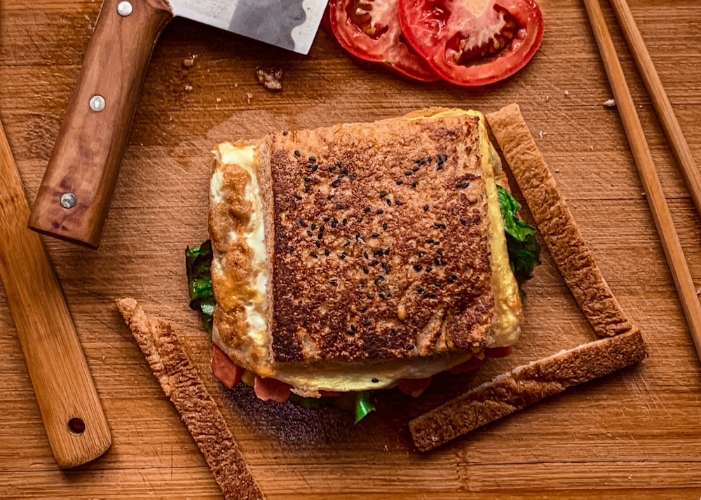 a sandwich on a cutting board with a knife and tomatoes