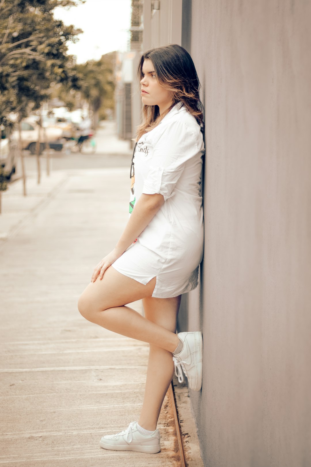woman in white shirt and white short shorts leaning on white wall