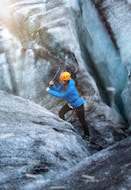 man in blue t-shirt climbing on gray rock