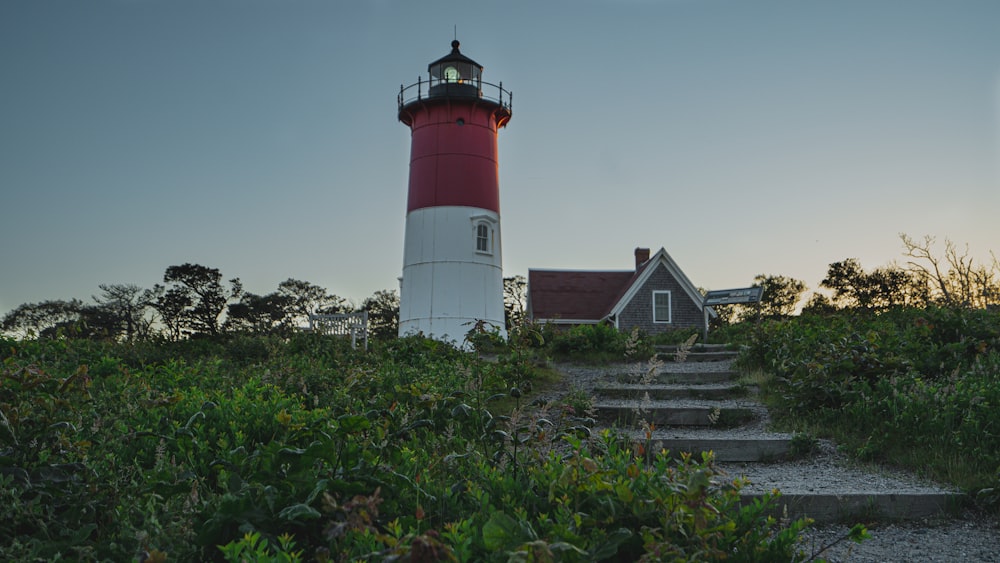 farol vermelho e branco perto da casa branca sob o céu azul durante o dia