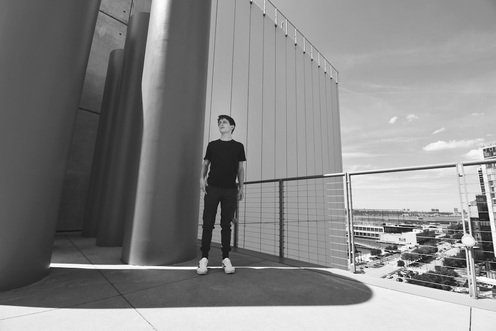 grayscale photo of man in black t-shirt and black pants standing on bridge