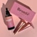 A pink-themed arrangement featuring a skincare bottle labeled 'Bronte Body Glow' placed beside a matching pink box. A rose gold razor and a pink-handled razor are also positioned nearby, casting distinct shadows on a pink surface.