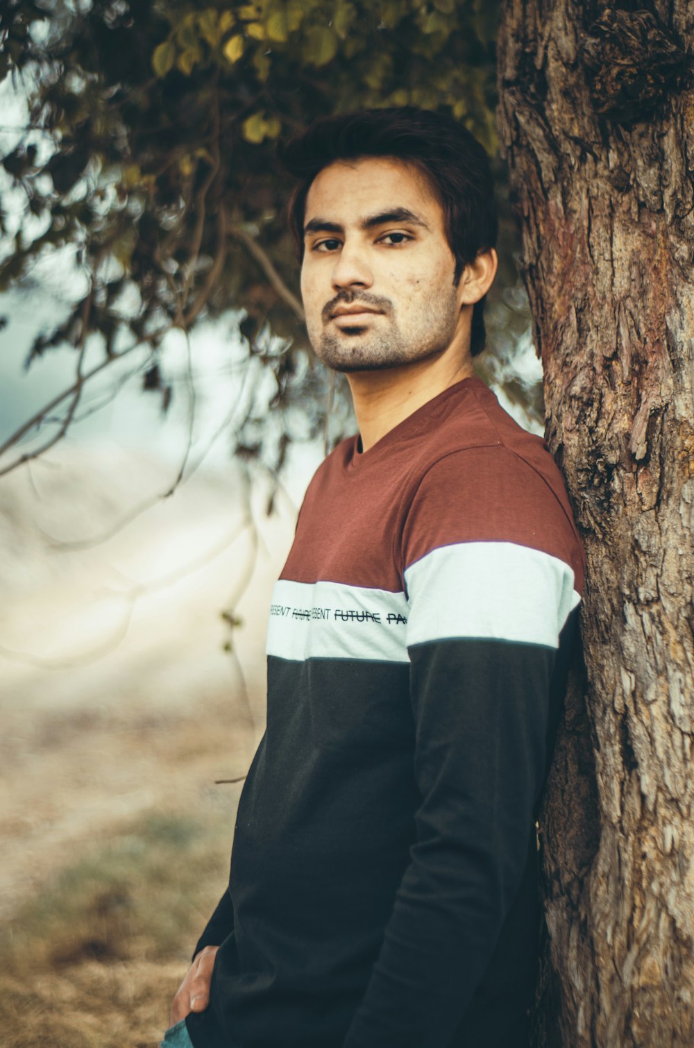 man in red and white shirt standing beside brown tree