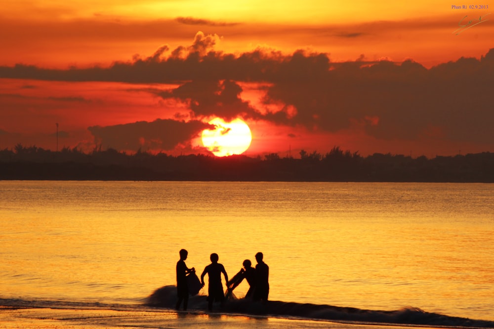 silhouette of people sitting on rock near sea during sunset