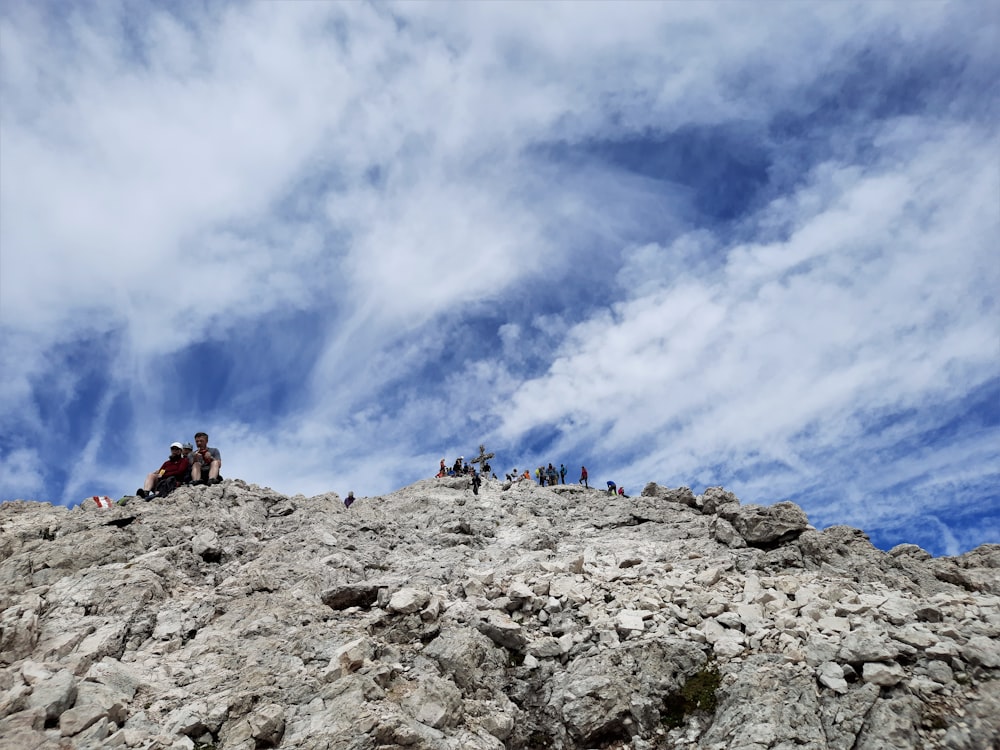people hiking on rocky mountain under white clouds and blue sky during daytime