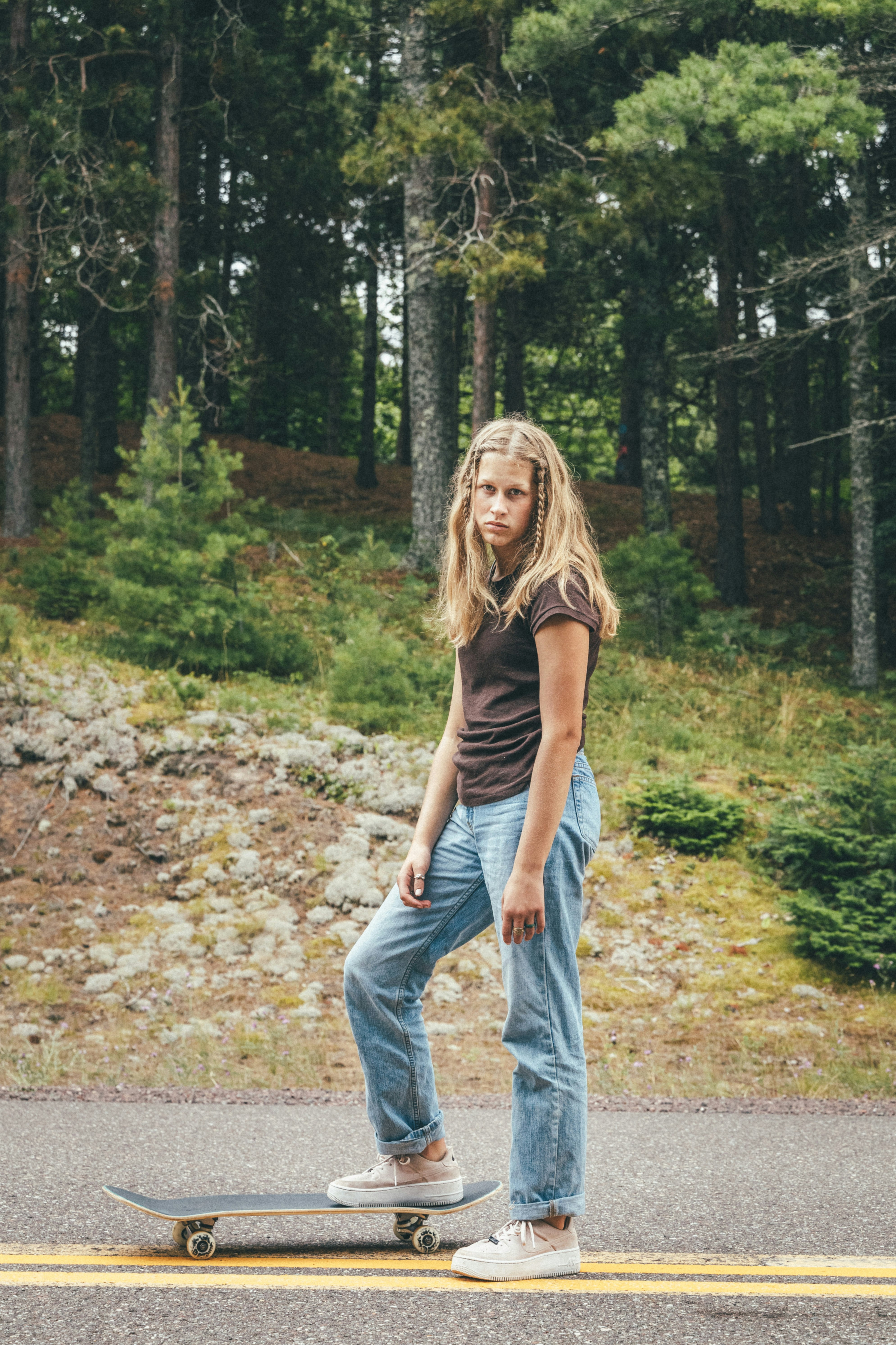 woman in gray tank top and blue denim jeans standing on brown dried leaves during daytime