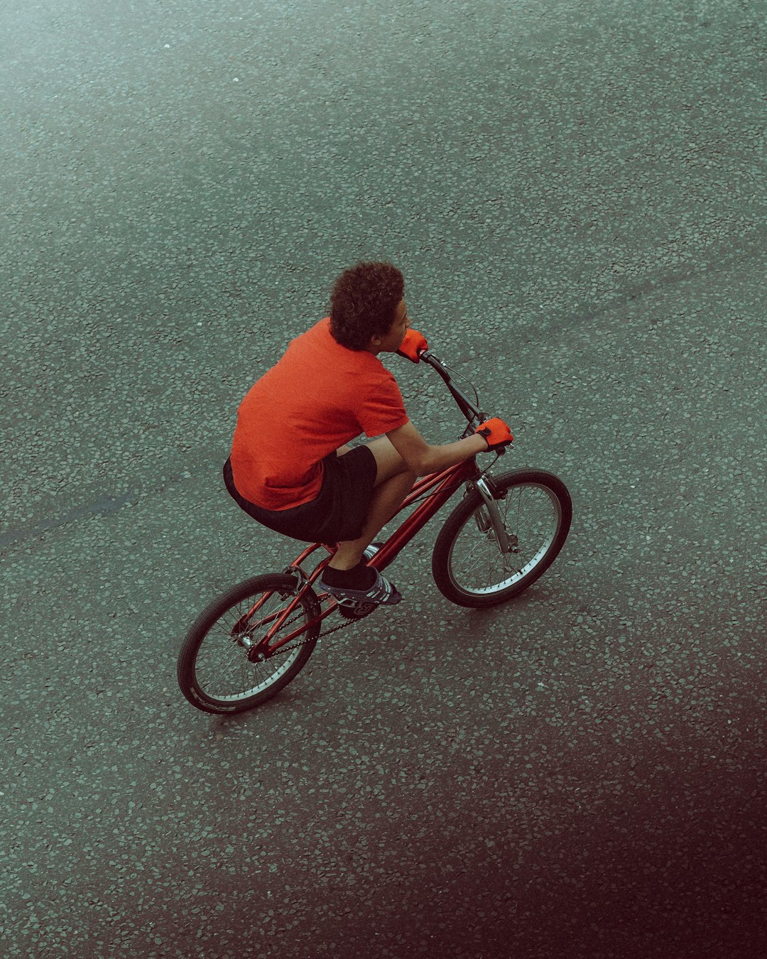 man in red shirt riding on bicycle on gray asphalt road during daytime