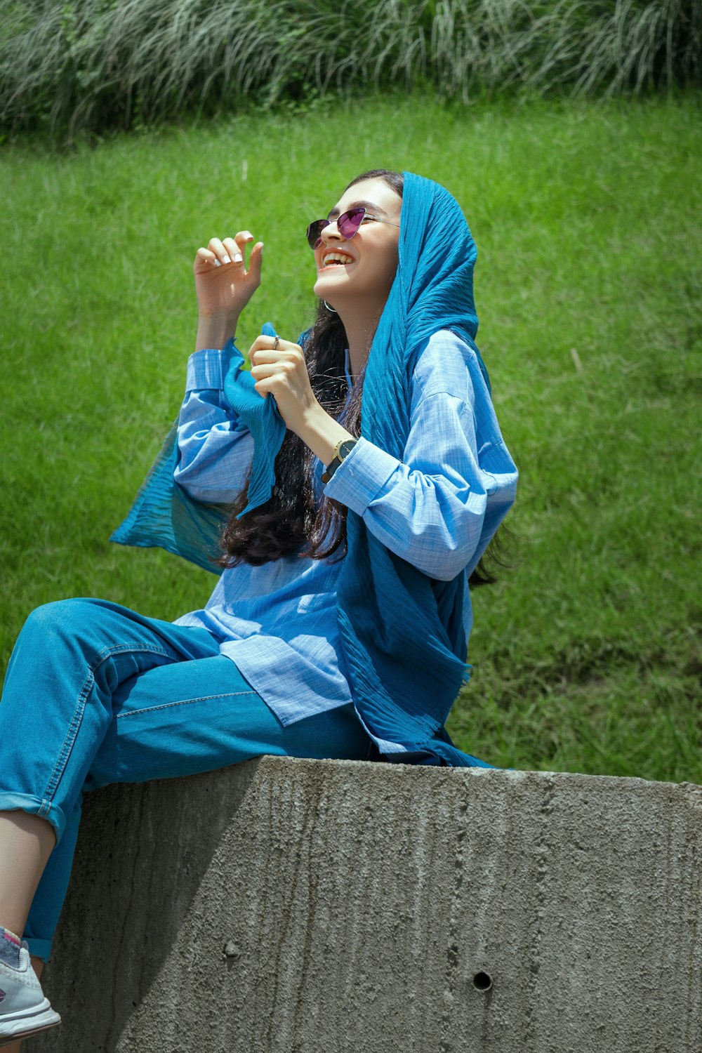 mulher no hijab azul e camisa branca de manga comprida sentada no banco de madeira marrom durante o dia