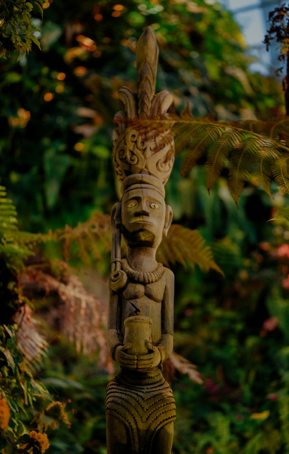 brown wooden statue near green plants during daytime