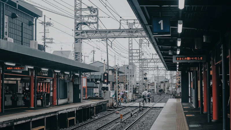 A quiet local railway platform in Japan, tracks and overhead wires running into the distance